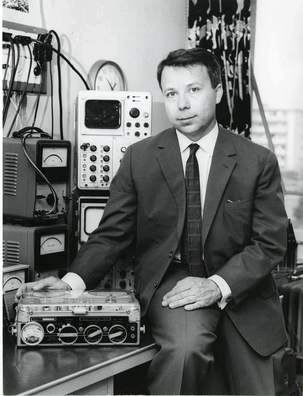 Stefan Kudelski in a suit sitting in front of electronic equipment and a tape recorder.