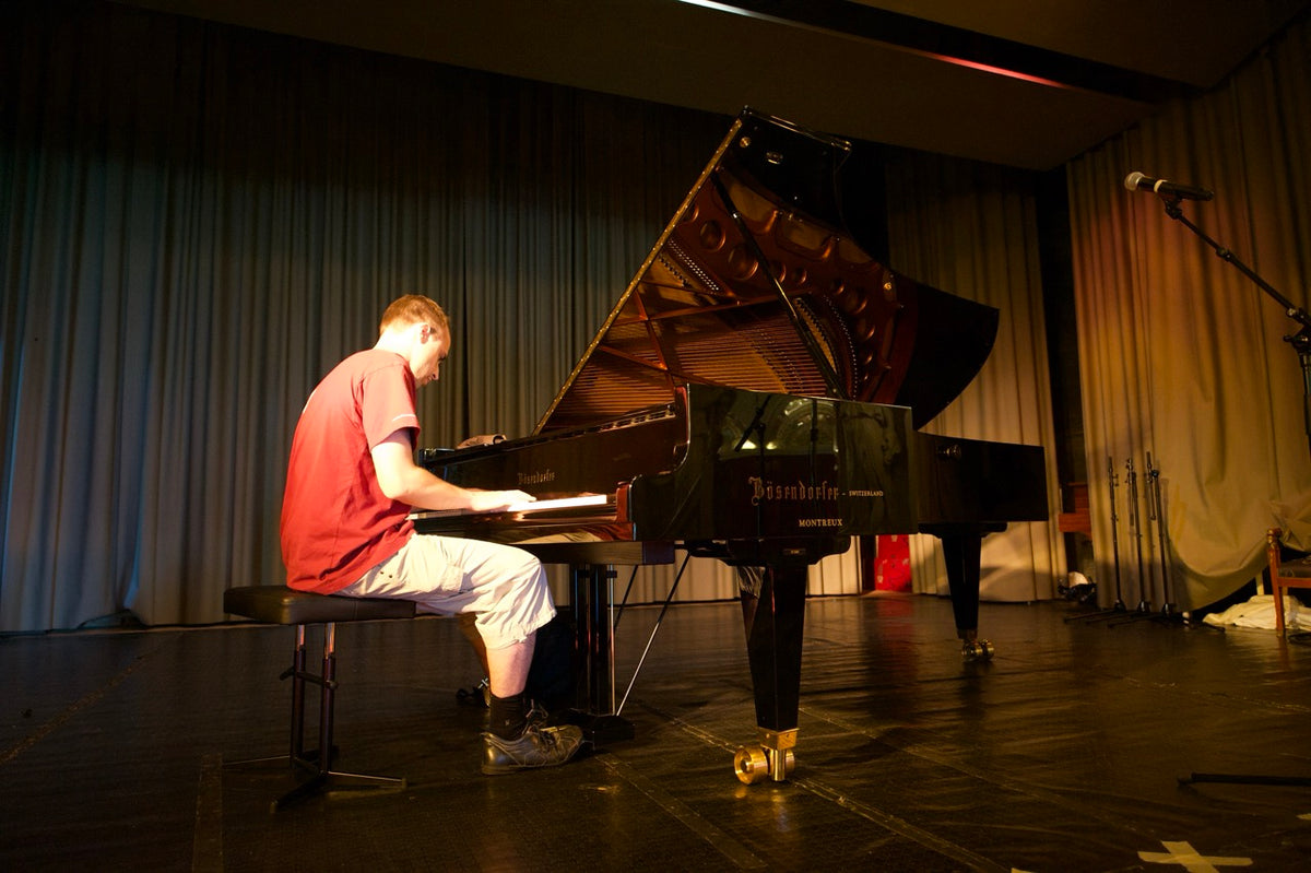 Person playing a grand piano on a stage with curtains in the background