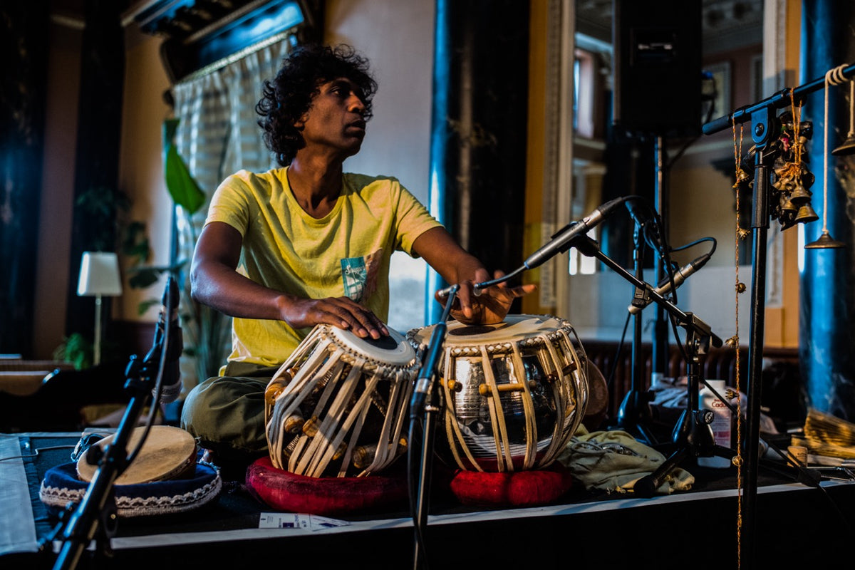 Person playing a tabla in a room with musical equipment