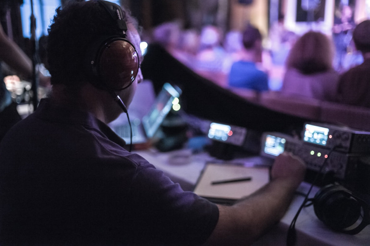 Person operating audio equipment in a control room with blurred audience in the background