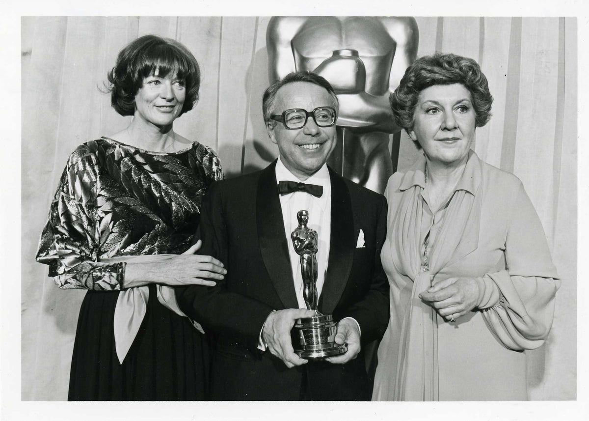 Black and white photograph of a Stefan Kudelski holding an Oscar with two women on either side.