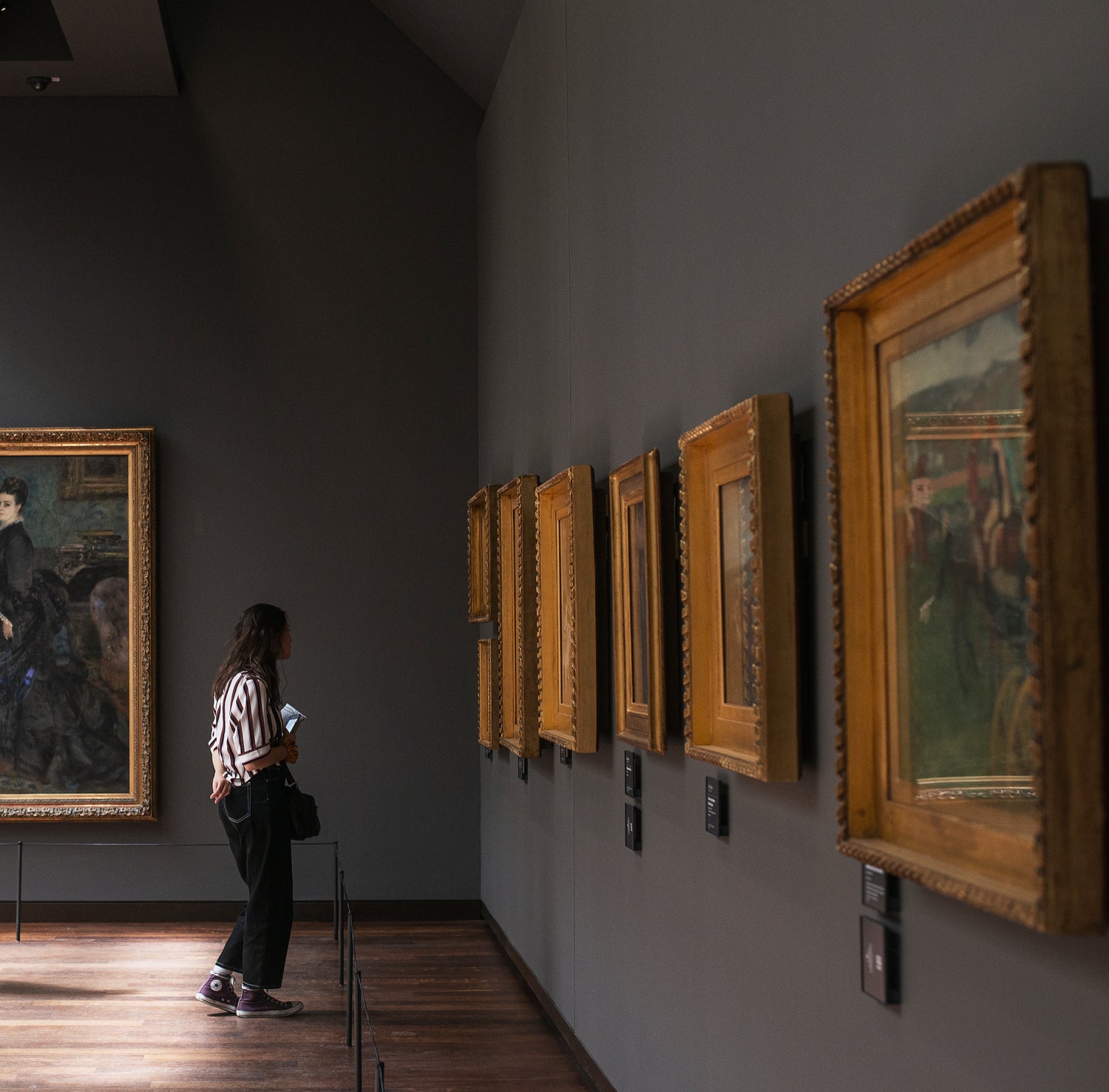 A woman stands in a museum looking at fine art